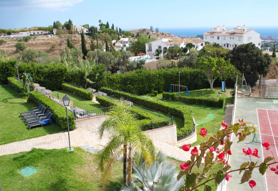 a lush green garden with a winding path and lush vegetation , overlooking a beautiful view of the ocean at Ilunion Hacienda de Mijas