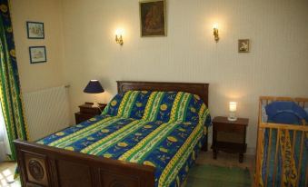 a cozy bedroom with a wooden bed , blue and green bedding , two lamps on the wall , and a painting above the bed at L'Horizon