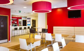 a modern dining area with red walls , white chairs , and wooden tables under red pendant lights at Travelodge Norwich Central Riverside
