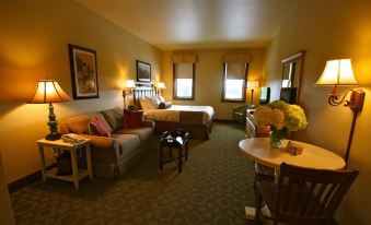 a well - lit hotel room with a bed , couch , and dining table , all arranged in a cozy setting at Homestead Resort