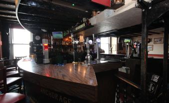 a bar with a long wooden counter and several bottles of alcohol on display , along with chairs and tables at The Anchorage Hotel