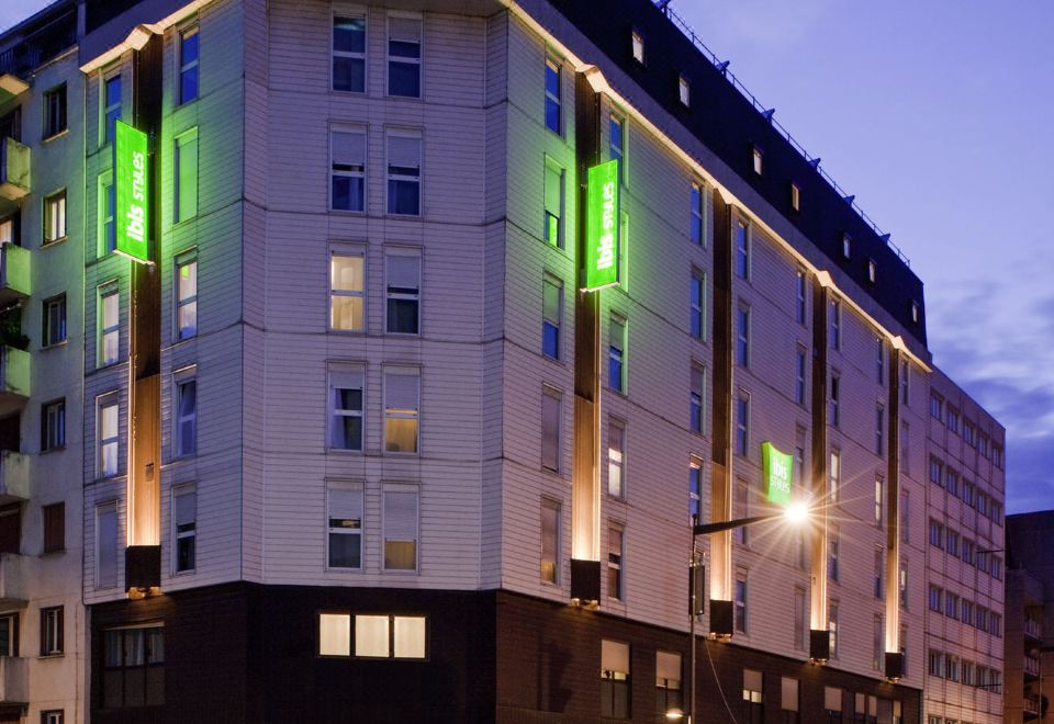 a large building with a green and white exterior is lit up at night , located on a city street at Ibis Styles Paris Mairie de Montreuil