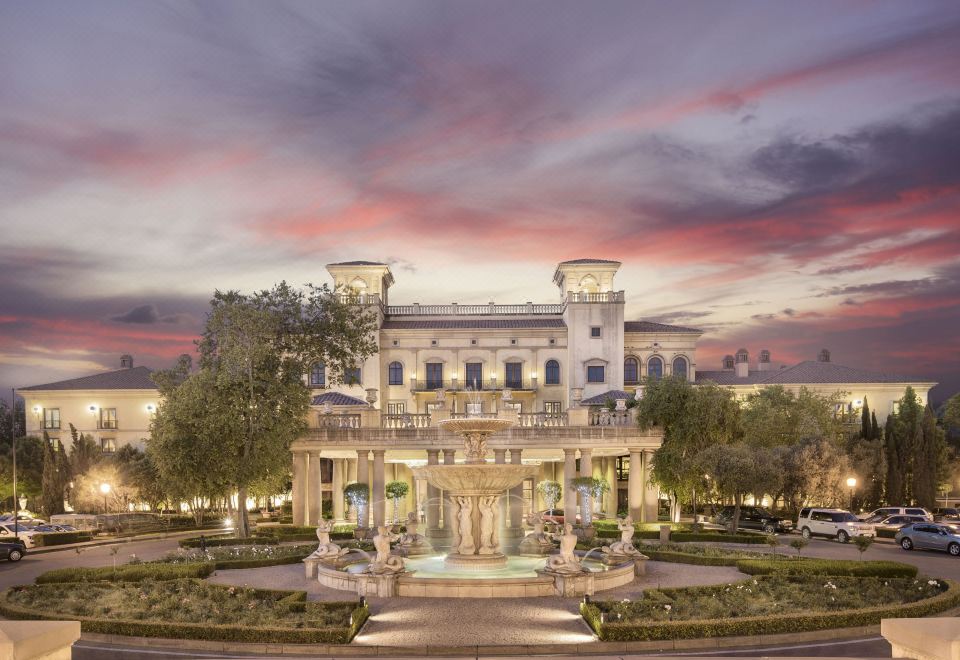 a large , ornate building with a fountain in front of it , surrounded by trees and a park at Palazzo Hotel