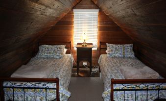 a cozy bedroom with two beds , each equipped with bedding and pillows , under a wooden slanted ceiling at Westbury Gingerbread Cottages