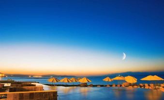 a serene beach scene with multiple yellow umbrellas and tents , a pool , and the moon in the sky at Djibouti Palace Kempinski