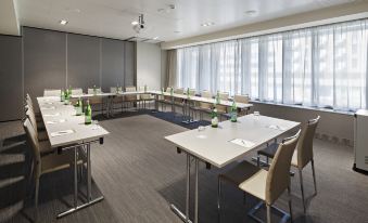 a conference room with a long table set up for a meeting , chairs arranged in rows , and a projector mounted on the wall at NH Parma