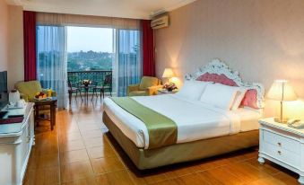 a large bed with a white and green comforter is in the middle of a room with wooden floors and a sliding glass door at Braja Mustika Hotel Bogor