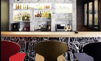 a modern bar with a black and white patterned wall , shelves filled with bottles , and two chairs placed next to it at Ibis Strasbourg Centre Historique