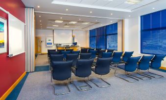 a conference room with chairs arranged in rows and a projector screen on the wall at Holiday Inn Express Milton Keynes