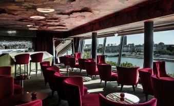 a modern lounge area with red chairs and a large window overlooking a body of water at Sofitel Lyon Bellecour