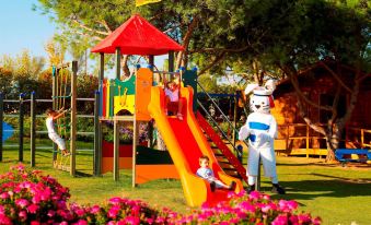 a group of children playing on a colorful playground with a bear mascot dressed as a pilot at Vila Alba Resort