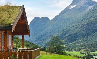 a wooden cabin with a thatched roof sits on a grassy hillside , surrounded by mountains in the background at Olden