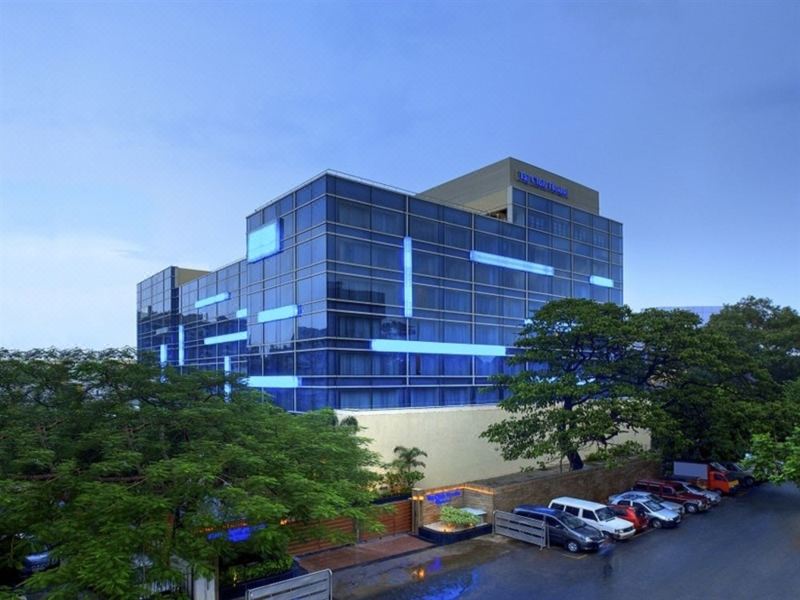 a modern building with blue and white lights on the exterior , surrounded by trees and parked cars at Taj Club House