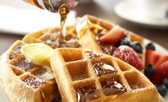 a plate of waffles with syrup being poured over , accompanied by a cup of coffee at Country Inn & Suites by Radisson, Watertown, SD