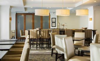 a modern , well - lit dining area with beige chairs and tables , large windows , and pendant lights at Hampton Inn Hallandale Beach-Aventura