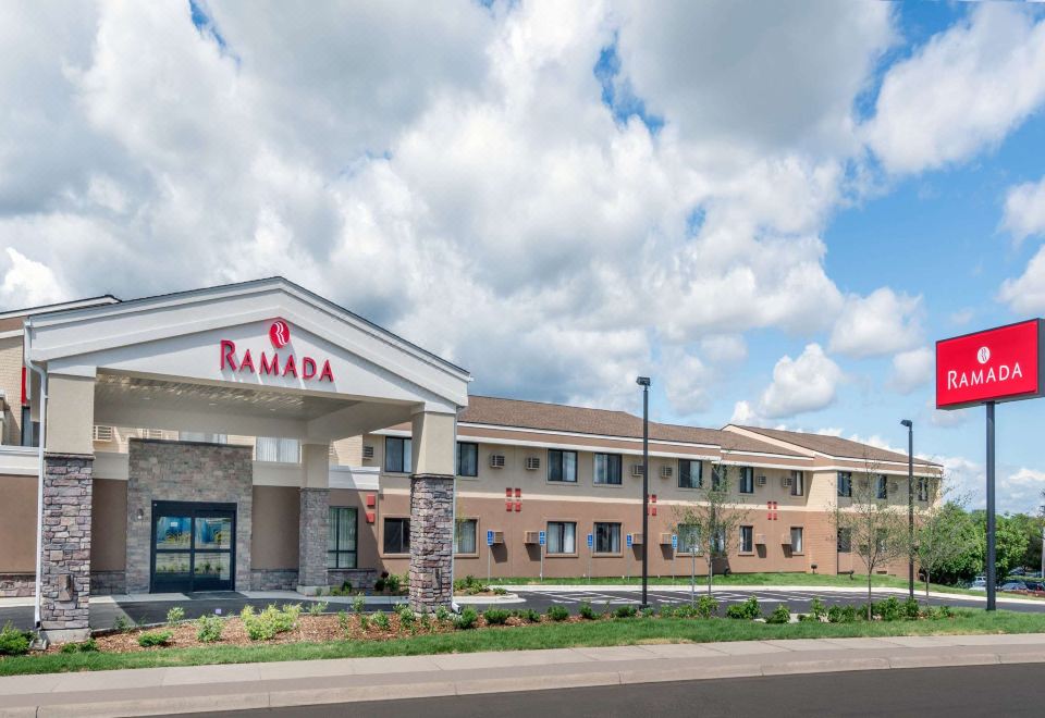 "a large , white building with a red sign that says "" ramada "" is surrounded by trees and a road" at Ramada by Wyndham Minneapolis Golden Valley