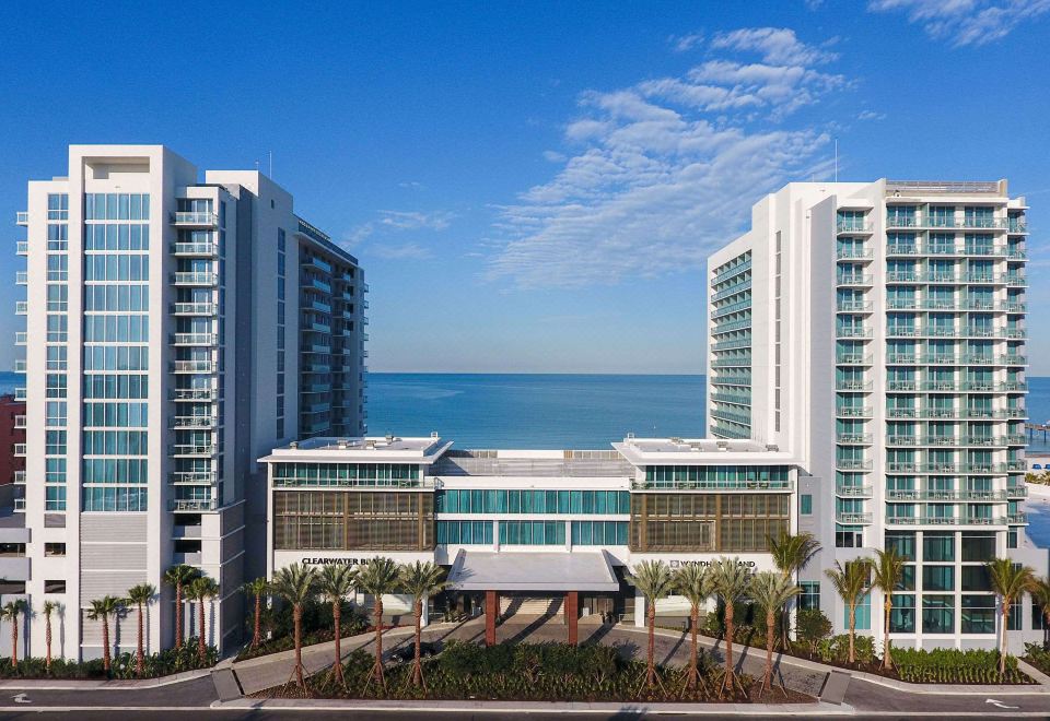 a modern building with multiple floors , surrounded by palm trees and a view of the ocean at Wyndham Grand Clearwater Beach