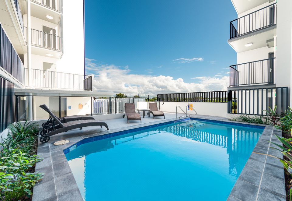 a large swimming pool with lounge chairs and a balcony is shown in front of a building at Pacific Sands Apartments Mackay