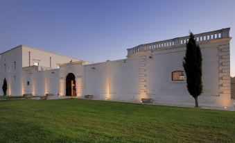 a large white building with a grassy field in front of it , illuminated by lights at Masseria Amastuola Wine Resort