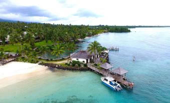 a boat is docked near a small hut on a waterfront with palm trees and buildings at Sinalei Reef Resort & Spa
