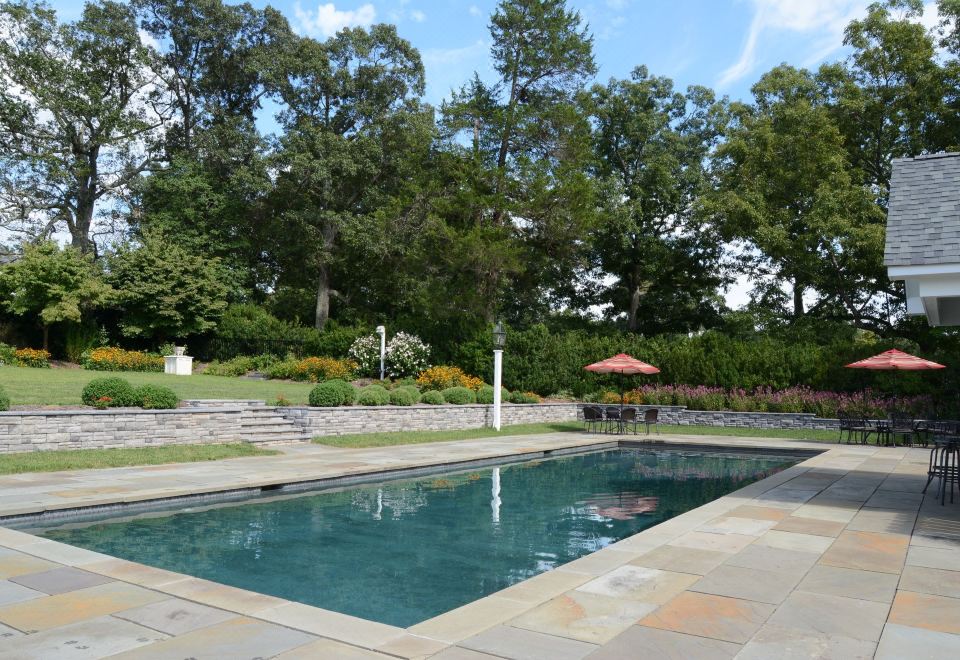 a large swimming pool surrounded by trees and a stone wall , with a red umbrella placed near the pool at Woodville Bed and Breakfast