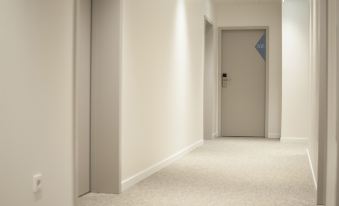 a long hallway with white walls and a carpeted floor , leading to a door at the end at Bayerischer Hof