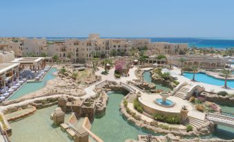 aerial view of a resort with a pool surrounded by multiple buildings , including a hotel and a beach at Kempinski Hotel Soma Bay