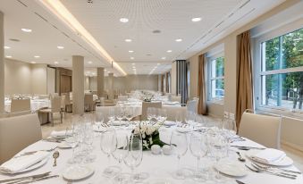 a large dining room with white tables and chairs , set for a formal event , and a centerpiece of flowers at NH Madrid Nacional
