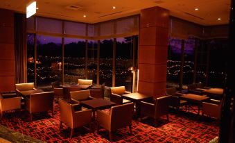 a modern , well - lit lounge area with wooden furniture and large windows offering views of the city at night at Hiroshima Airport Hotel