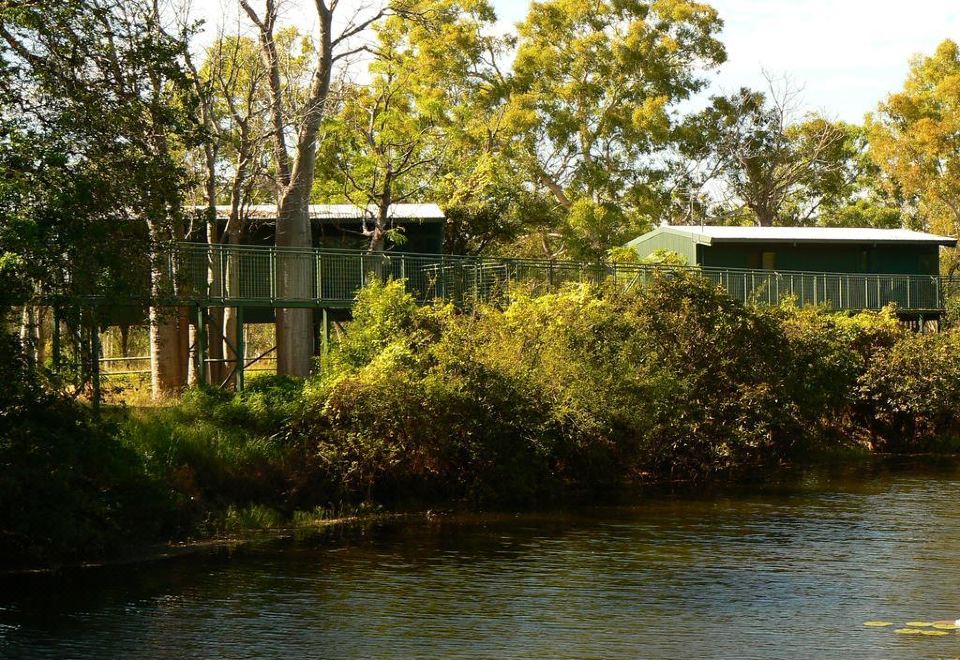 a river with trees and a bridge , and several buildings in the background , including one house with a red roof at Parry Creek Farm Tourist Resort & Caravan Park