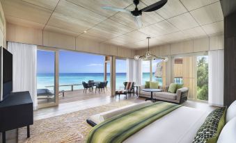 a spacious bedroom with a large bed and sliding glass doors leading to an ocean view balcony at The St. Regis Maldives Vommuli Resort