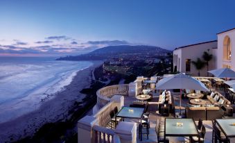 a rooftop dining area with tables and chairs , overlooking the ocean and beach at sunset at The Ritz-Carlton, Laguna Niguel