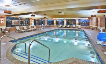 an indoor swimming pool surrounded by lounge chairs , with people enjoying their time in the pool area at Holiday Inn Manitowoc