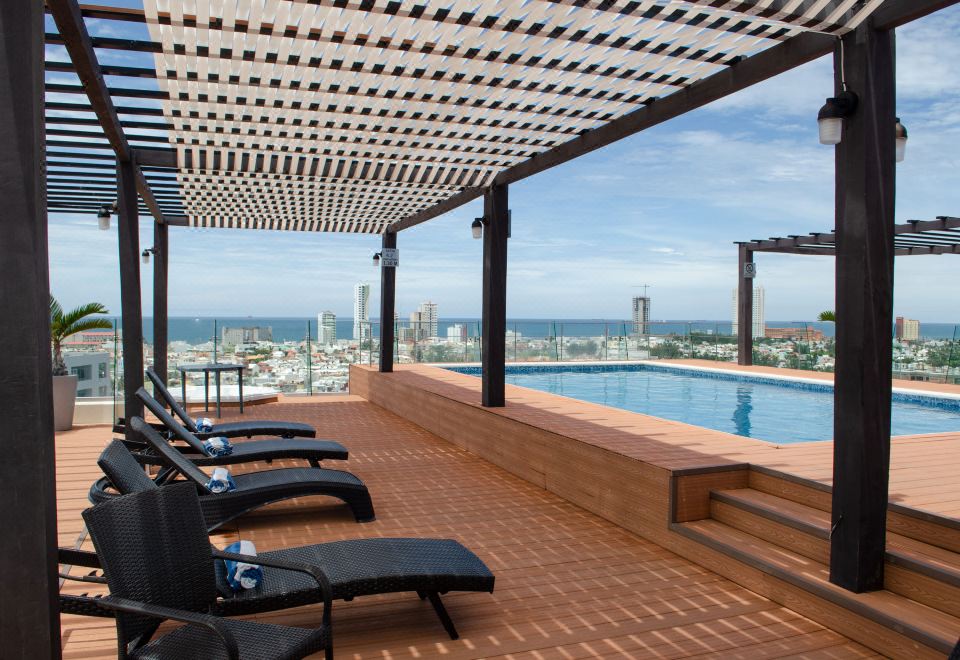 a rooftop patio with a swimming pool surrounded by lounge chairs , and a view of the city skyline at Four Points by Sheraton Veracruz