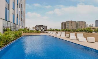 a large swimming pool with white lounge chairs is surrounded by tall buildings and trees at Park Inn by Radisson North Edsa