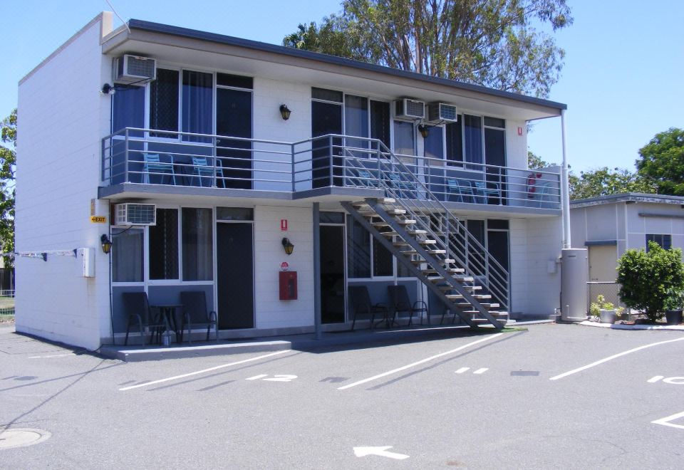 a two - story building with a staircase leading to the second floor and a parking lot in front of it at Motel Lodge