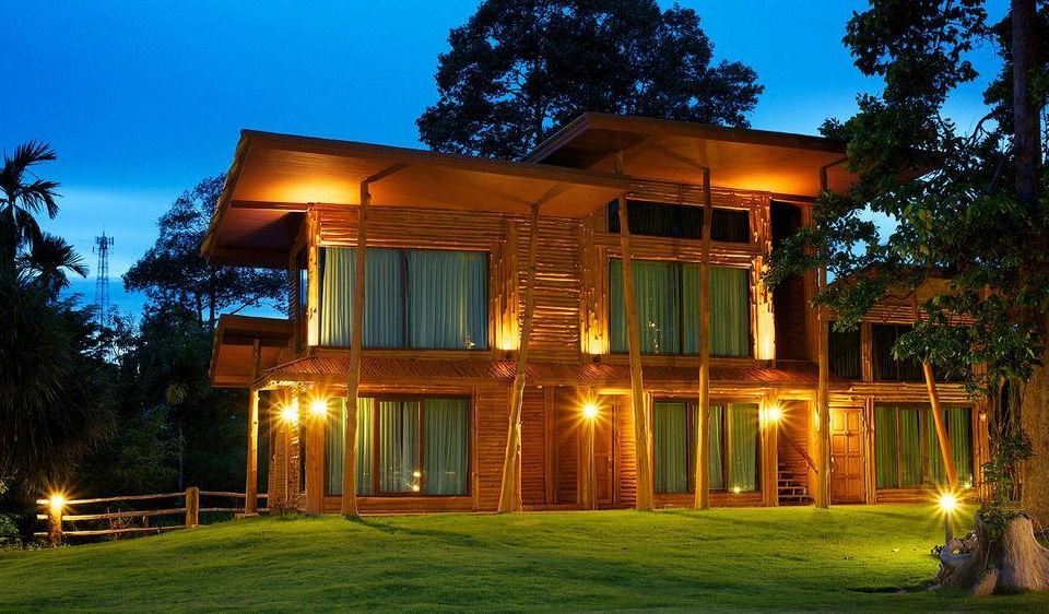 a large , modern wooden house with multiple windows and doors , lit up at night , surrounded by green grass and trees at Blues River Resort