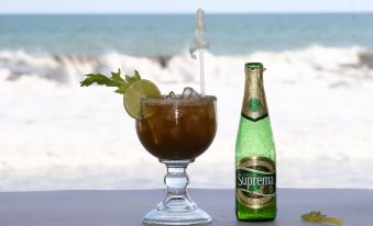 a glass of drink with a lime slice and a bottle of supreme beer on a table near the ocean at Hotel Estero y Mar