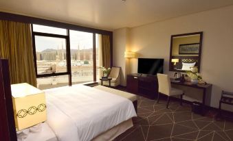 a large , well - lit hotel room with a bed , desk , and tv , as well as a balcony view of the city at Pullman Zamzam Madina