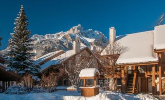 a snow - covered yard with a wooden gazebo , surrounded by a house and mountains in the background at Banff Rocky Mountain Resort