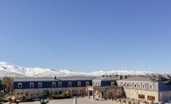 a large building with a blue roof is surrounded by mountains and has a plaza in front of it at Parador de Gredos