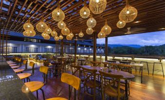an empty restaurant with wooden tables and chairs , surrounded by a view of the mountains at Plataran Heritage Borobudur Hotel