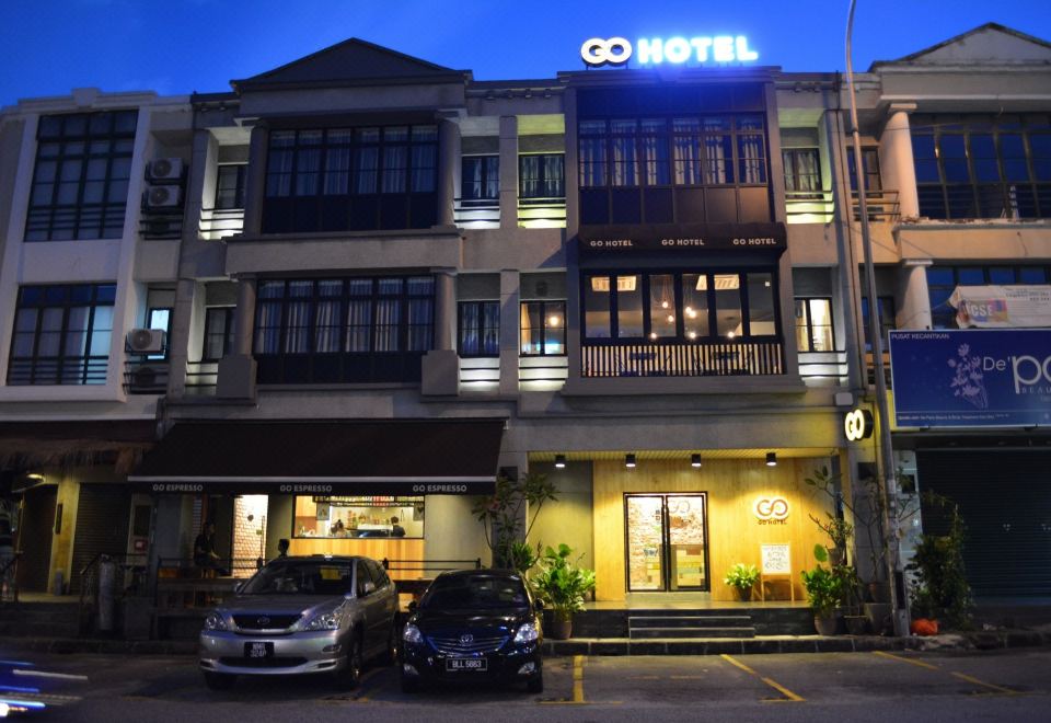 "a large building with a lit sign that says "" 0 0 hotel "" and two parked cars" at Go Hotel