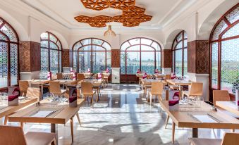 a modern , well - lit restaurant with wooden tables and chairs , large windows , and red pendant lights at Barcelo Isla Canela Hotel