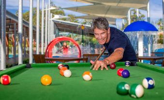 a man is playing a game of pool on a green pool table , surrounded by other people at Ingenia Holidays Lake Conjola