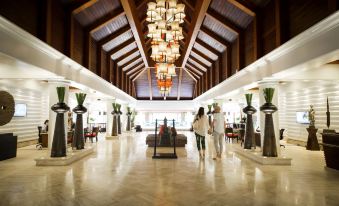a spacious , well - lit hotel lobby with a wooden ceiling and chandeliers , two people walking through the entrance at Robinson Khao Lak
