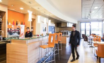 a modern office interior with wooden reception desks , orange chairs , and a man walking through the lobby at Ibis Como