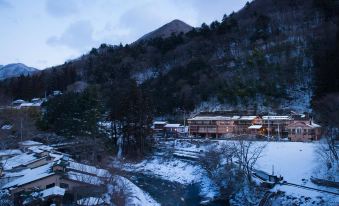 a snowy landscape with a mountain in the background and a river flowing through a village at Shima Onsen Kashiwaya Ryokan
