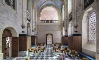 a grand interior with high ceilings , arches , and marble floors , featuring rows of wooden tables and chairs arranged in a spacious room at The Jaffa, a Luxury Collection Hotel, Tel Aviv