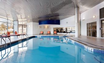 an indoor swimming pool with a blue tiled floor , surrounded by lounge chairs and a ceiling at Delta Hotels Woodbridge